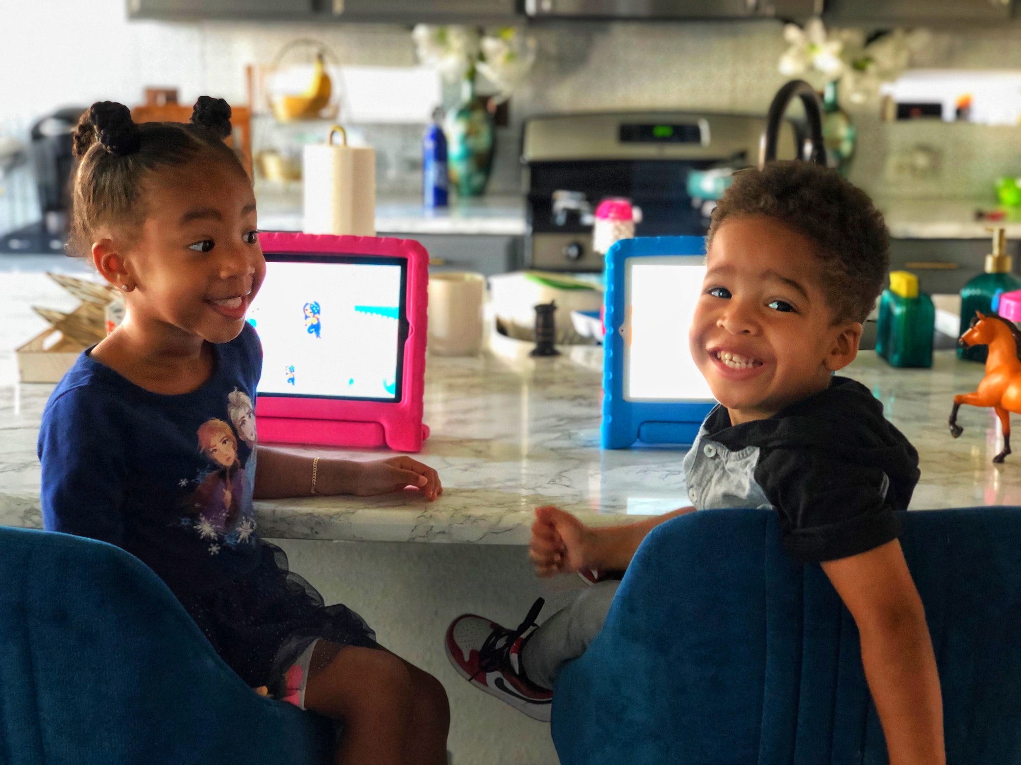 Two black toddlers, sitting at the kitchen counter,doing school online classes on iPads technology